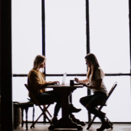 Woman typing on laptop and another woman writing on notepad while sitting across each other at the same table
