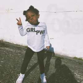 Female child making a V-sign with her fingers while wearing a sweatshirt with "Girl Power" printed across the chest
