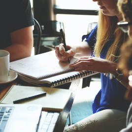Close-up of hands on a large table taking notes while a meeting takes place